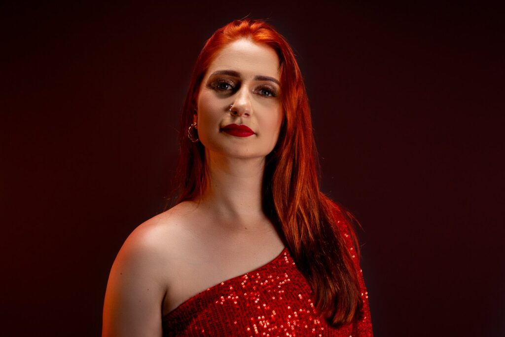 Retrato editorial de mulher ruiva com vestido vermelho brilhante sobre fundo vermelho escuro.