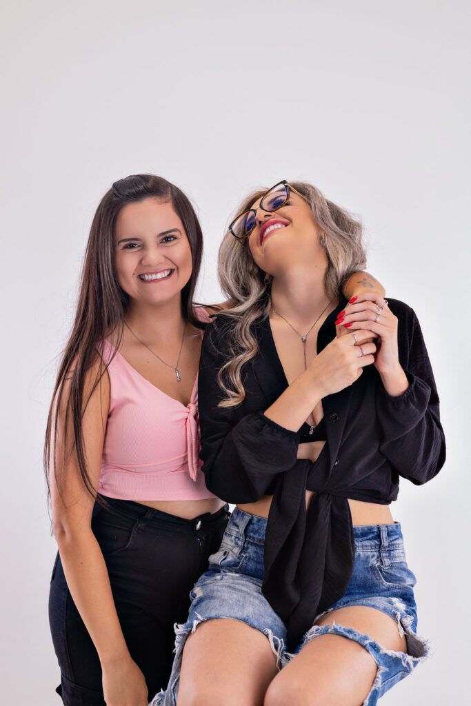 Duas amigas abraçadas e sorrindo durante um ensaio em estúdio.