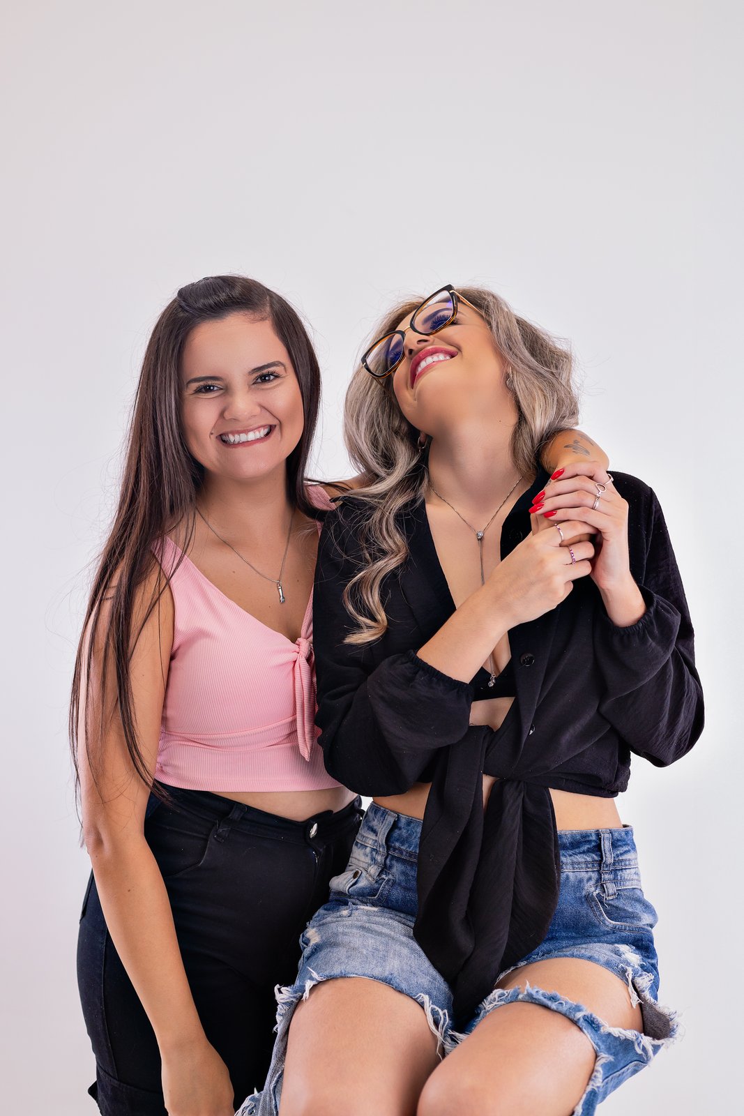 Duas amigas abraçadas e sorrindo durante um ensaio em estúdio.