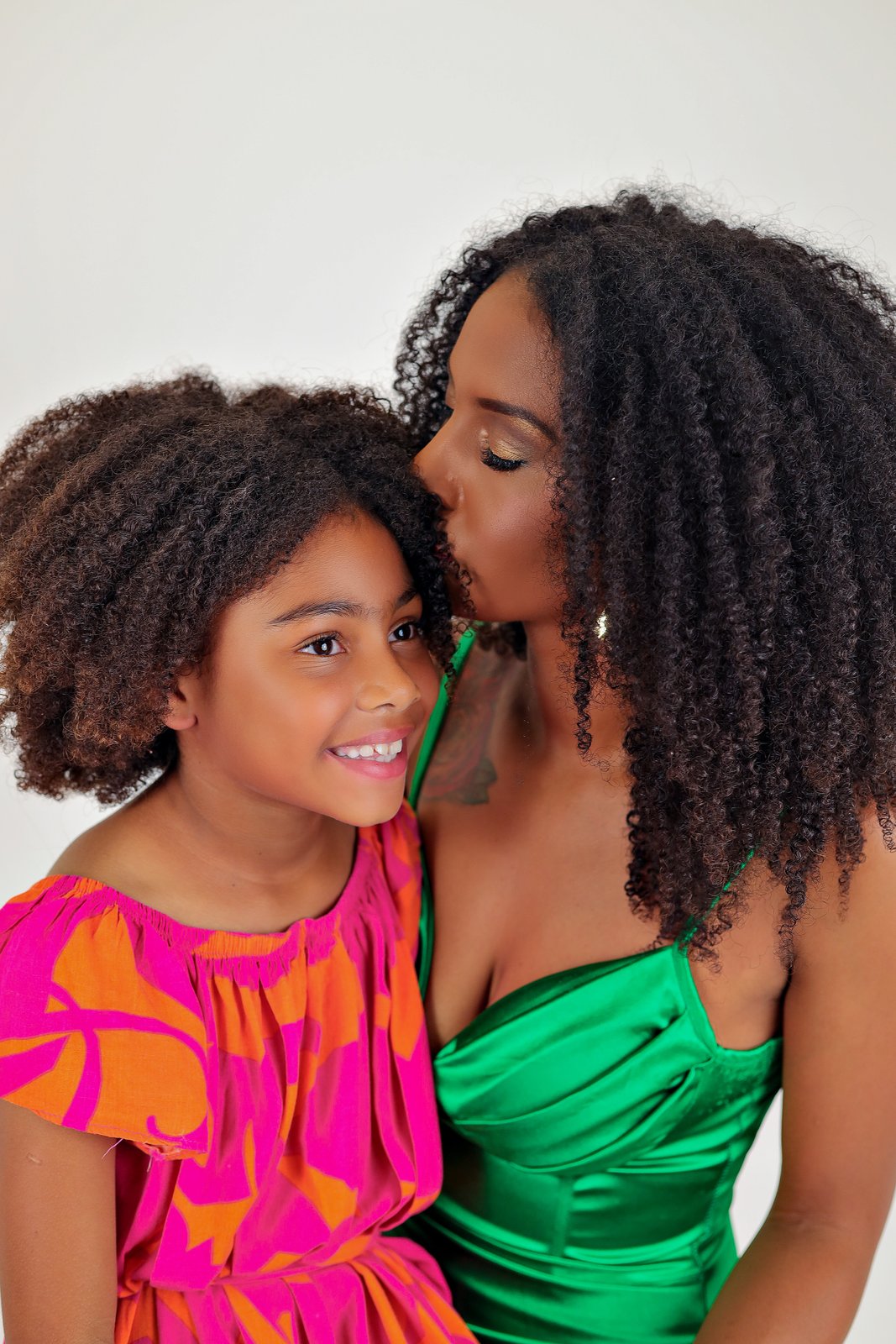 Mulher dando um beijo na testa de uma menina sorridente em um retrato de família.