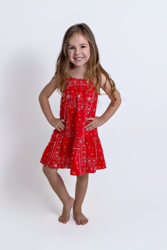 Menina sorrindo com vestido vermelho em ensaio infantil de estúdio.