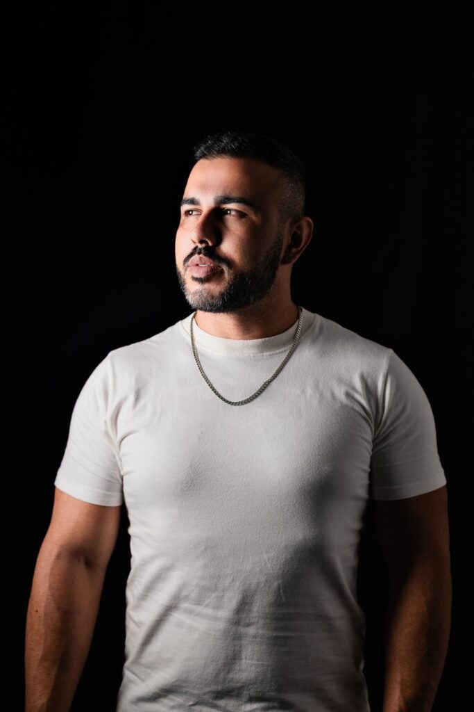 Homem de camiseta branca em retrato masculino com iluminação lateral e fundo escuro.
