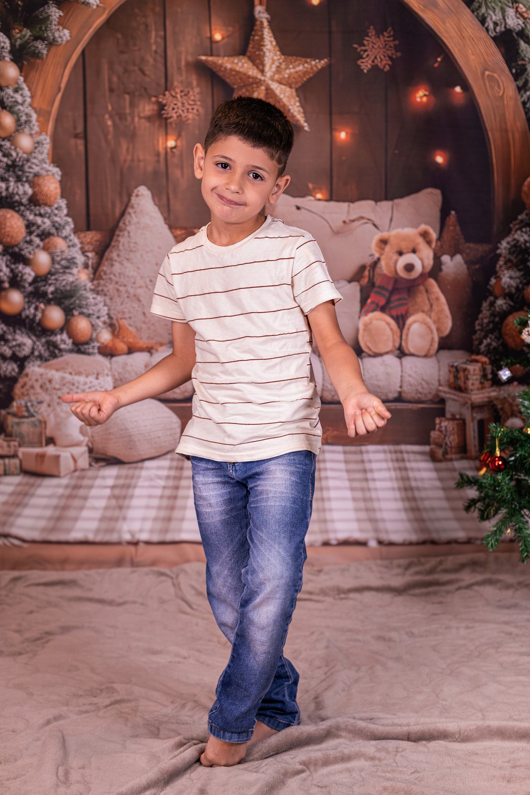 Menino posando em cenário de Natal com árvore, enfeites e estrelas.
