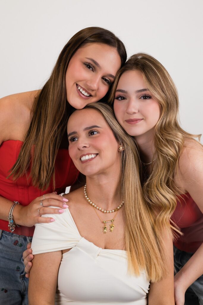 Três mulheres abraçadas em composição vertical, com blusas vermelhas e branca.